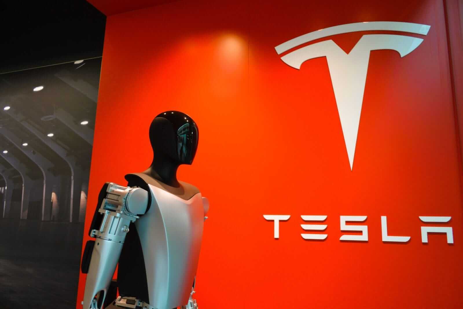 An image of a Tesla humanoid robot in front of the company logo Around the World Photos via Shutterstock